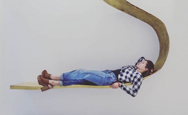portrait of designer Charlotte Kingsnorth lying on gold wall sculpture