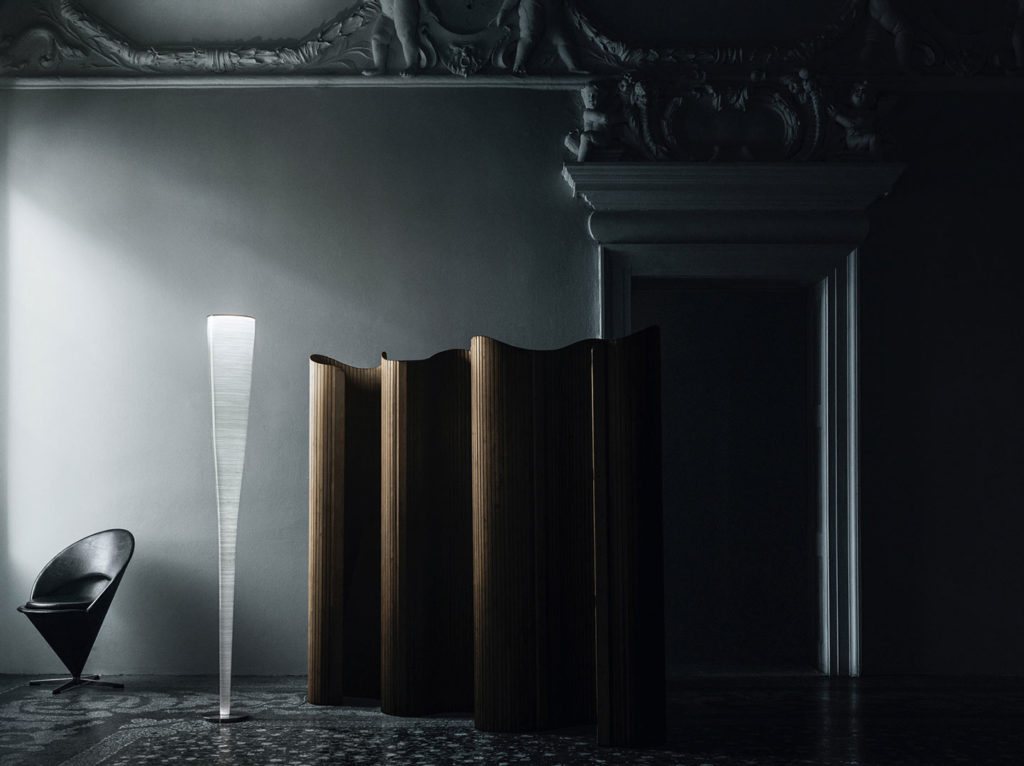 living room with tall sculptural white floor lamp, black chair, and room screen