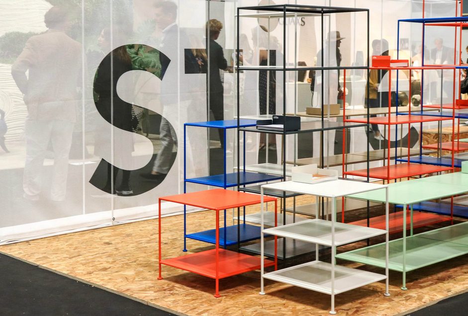 orange, blue, black, green, and white metal frame shelving on plywood floor in exhibit room