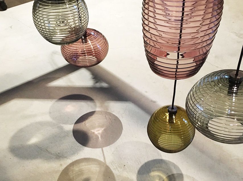 handblown glass pendants in different colors and shapes hanging above cement floor with shadows visible on floor
