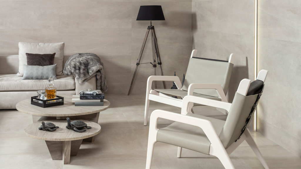 living room in neutral colors with modern couch, two lounge chairs, and coffee table, featuring tiled walls and floor