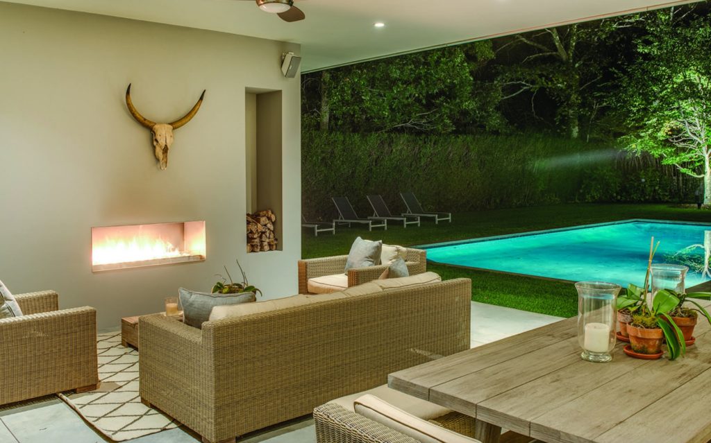 Modern Net Zero Hamptons' home interior view of living room with gas fireplace and wall to wall window with view of outdoor pool