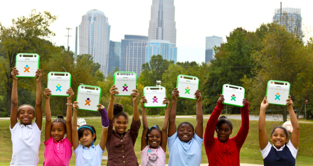 Yves Béhar One Laptop per Child many children of diverse ethnicities holding laptops overhead