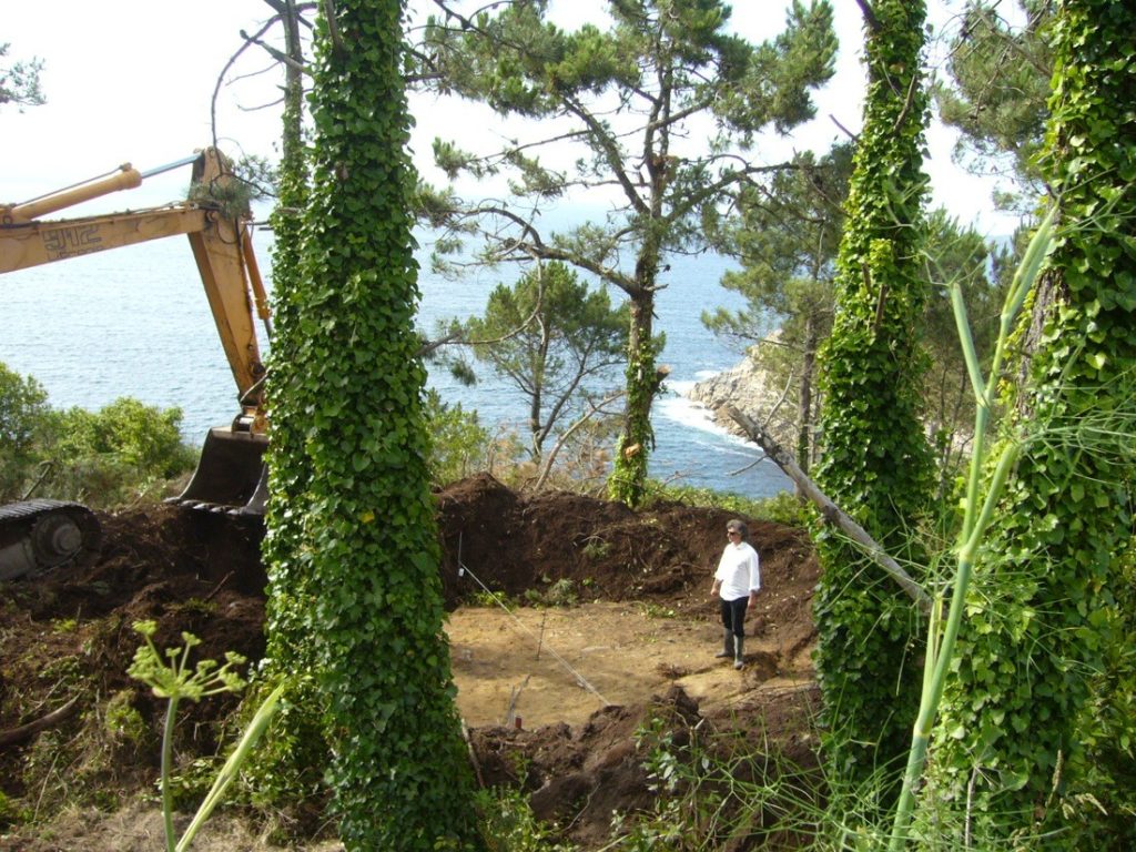 Truffle House Construction backhoe piling up earth with straw filling hole and man standing