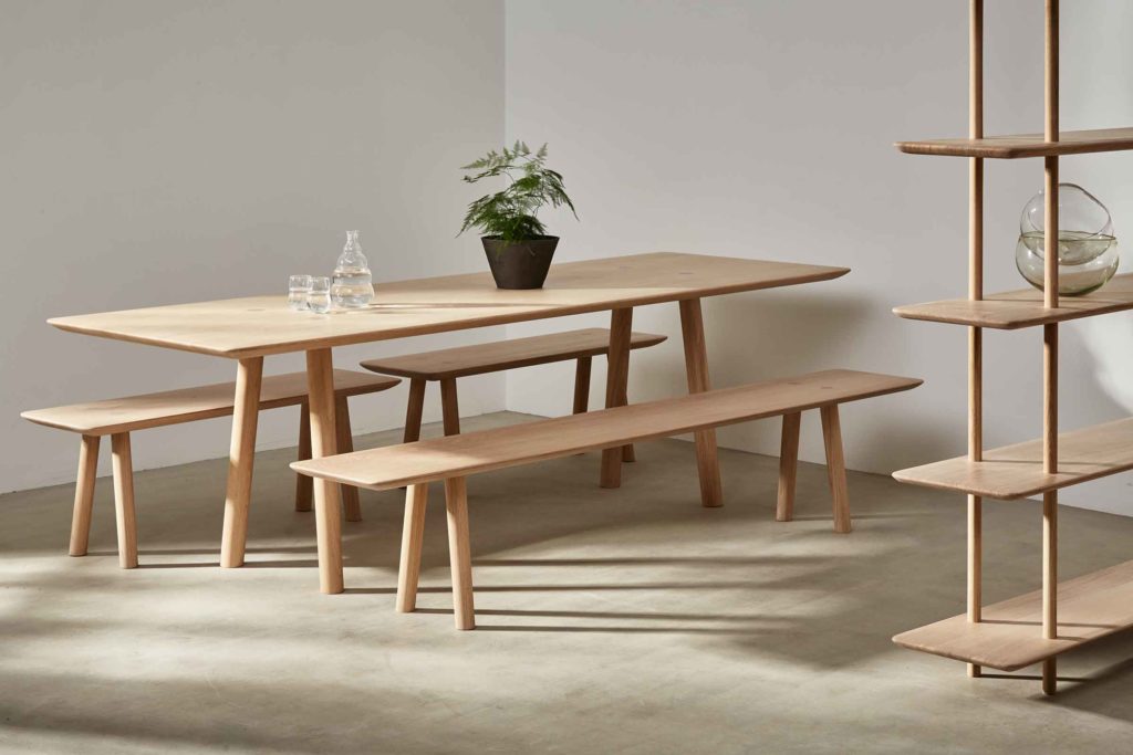 Benchmark Ovo Collection dining table with benches and partial view of shelving in light oak