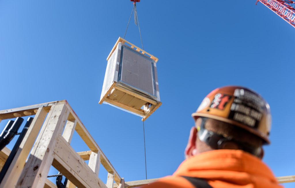 Katerra Bathroom Kit a boxed kit descending from a crane into room for installation with construction worker in foreground