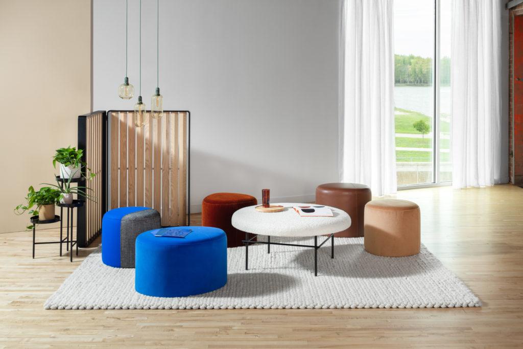 Allsteel Two-Thirds round and pebble poufs on white carpet with round table various colors in living room with wood floor