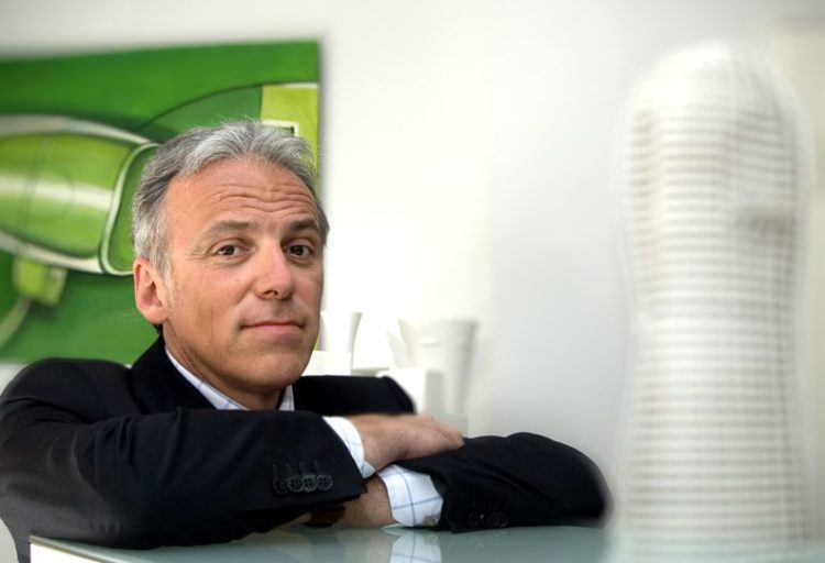 Massimo Iosa Ghini in dark suit with arms folded on table ledge