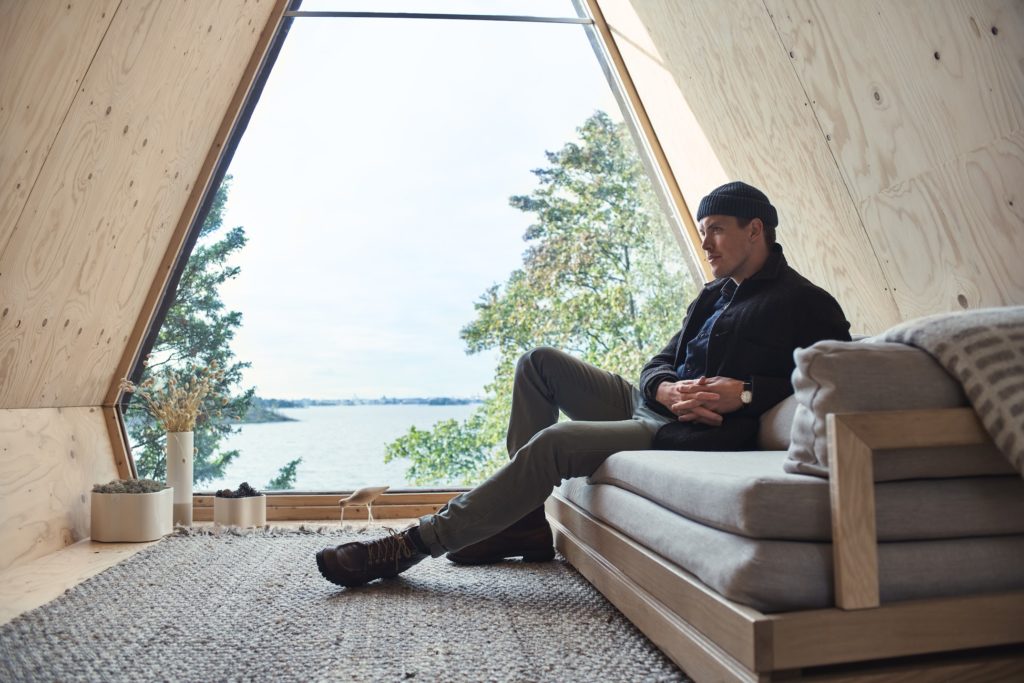 Zero Travel Nolla Cabin interior of cabin with designer Robin Falck seated on sofa and view to the outdoors