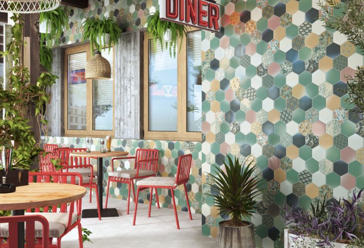 Tile of Spain 2020 designs Return to Color vibrant hexagonal tile in Mediterranean colors on outdoor wall of diner patio with wood tables and red chairs