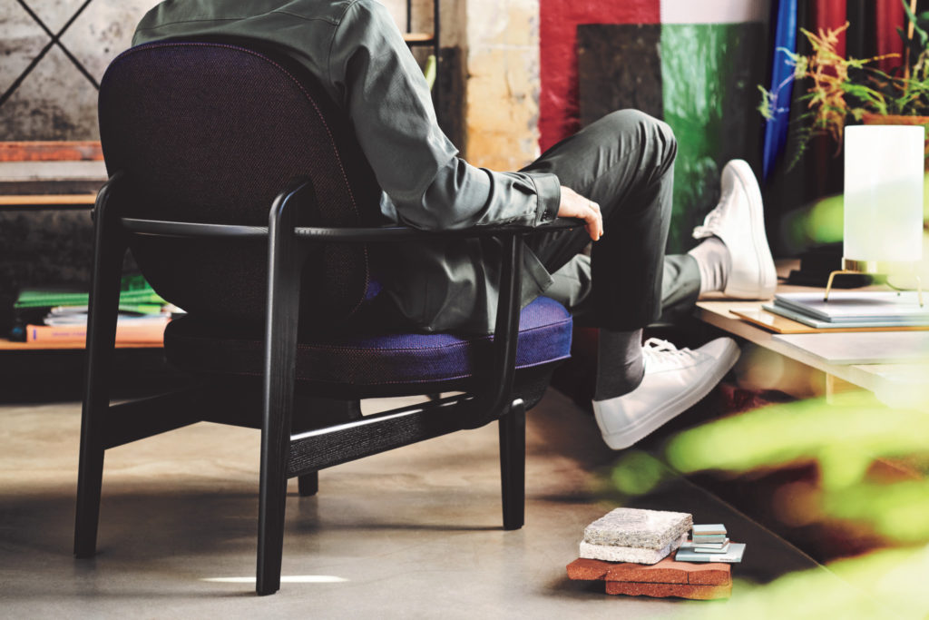 Fritz Hansen Fred Chair rear view in purple upholstery with man sitting and putting up shoes on storage table