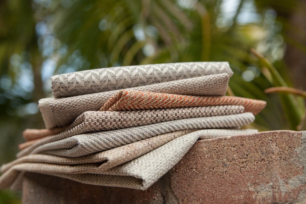 Architex Pure California Late Fall Collection detail of eight fabrics on brick wall with blurry tree in background