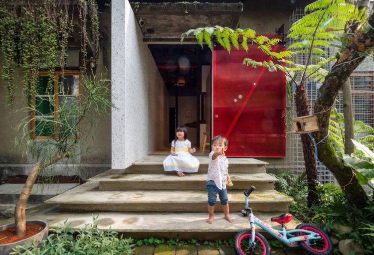 Living Lab Exterior Front two children with bicycle on front steps with open red door visible behind