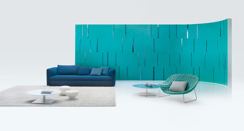 Paola Lenti Walt Seating blue sofa with teal room divider, white rug, low tables, and poufs