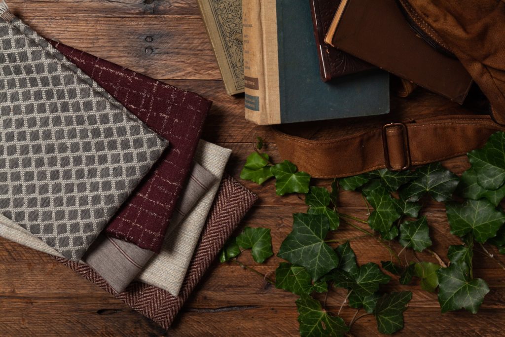 Architex Late Fall Collection Radcliffe Collection detail of five fabrics on table with holly branch and books