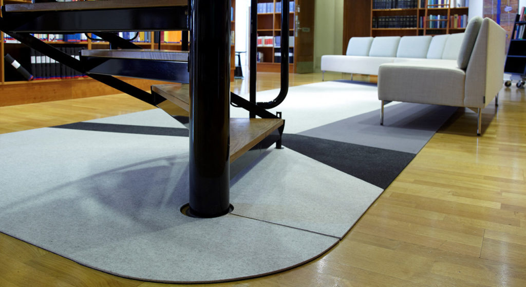 Fraster Felt Rug Collection gray rug with charcoal and black highlights/integrated shapes with sofa on top in room with bookshelves and spiral staircase