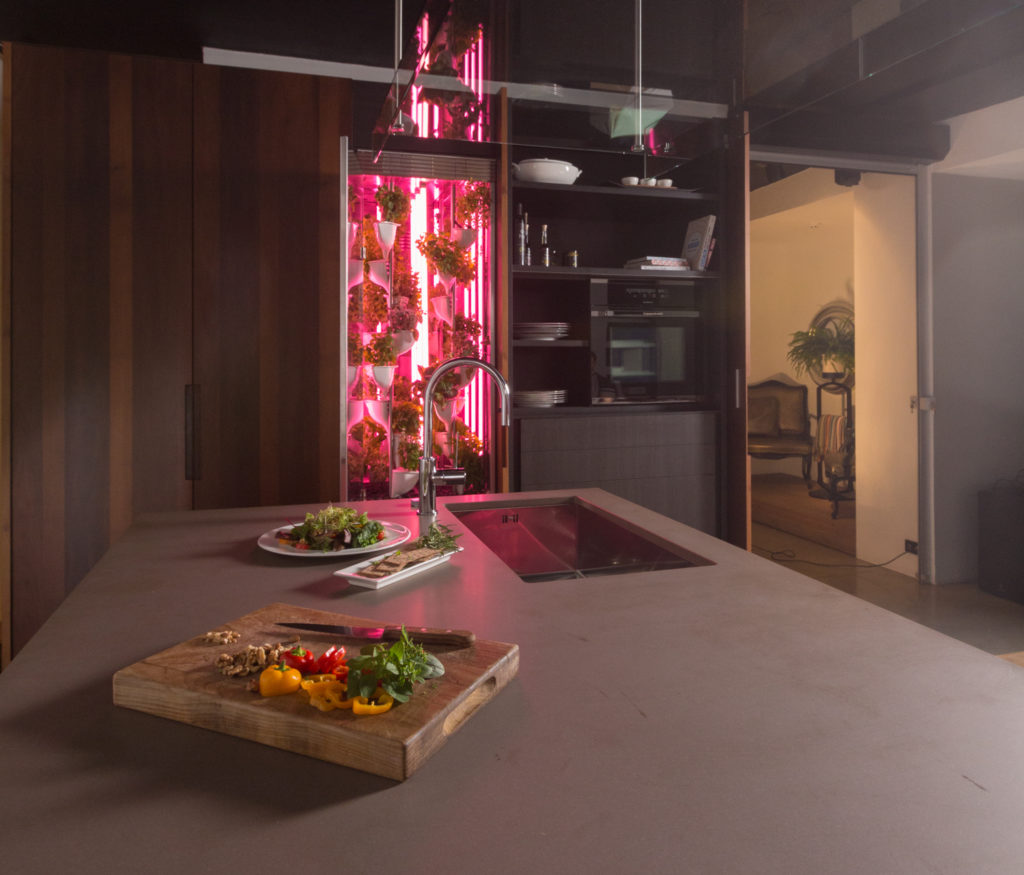 Natufia Kitchen Garden unit in background installed in kitchen with lights off and kitchen island in foreground with cutting board with chopped vaggies