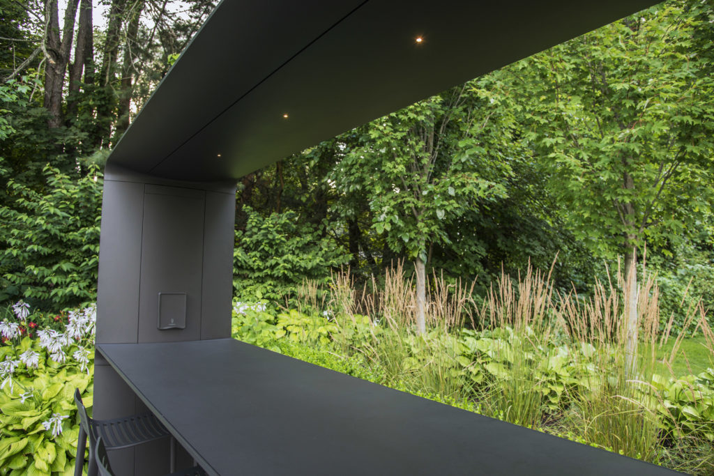 Landscape Forms' Go Outdoor Table standing height black with canopy in beautiful garden with lots of greenery