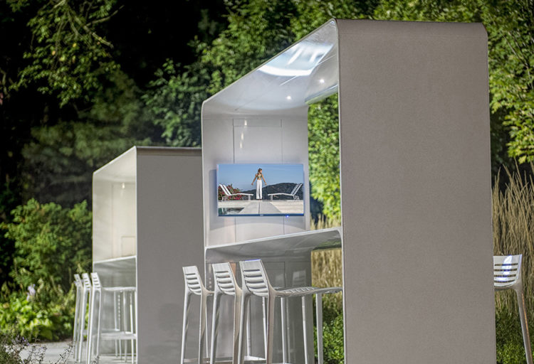 Landscape Forms' Go Outdoor Table two white standing height tables with canopy one with mounted monitor in beautiful garden setting