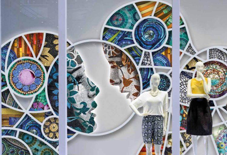 Batik Mosaics display in retail locale with different mosaics in the shape of two large heads and mannequins in foreground