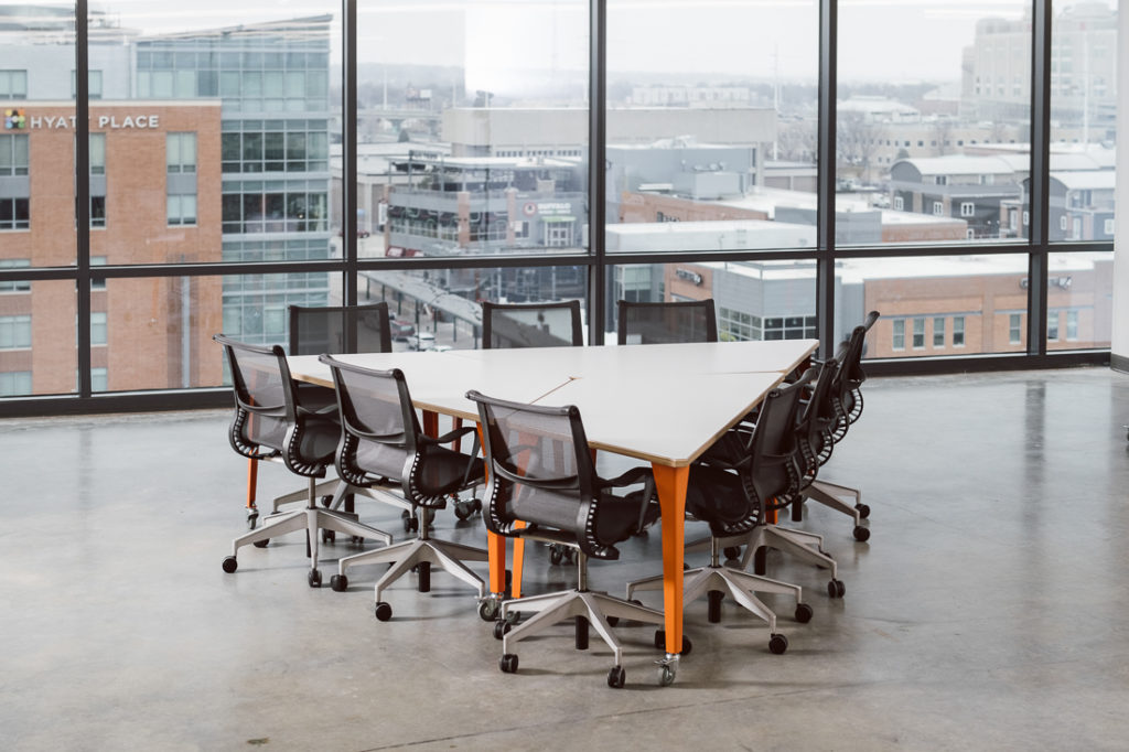 Werk Trap Table three tables with orange legs set together to form triangular shape surrounded by black taskk chairs in open room with view of city