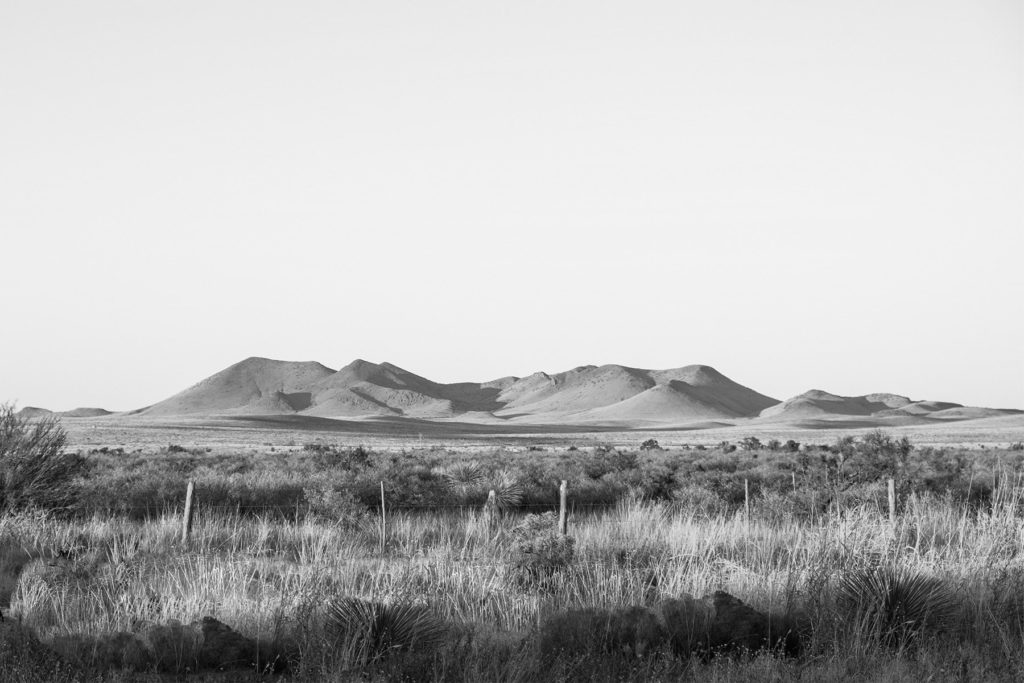 Image of landscape around Marfa, Texas with barbed wire fence, sagebrush, and sandy hills in the distance