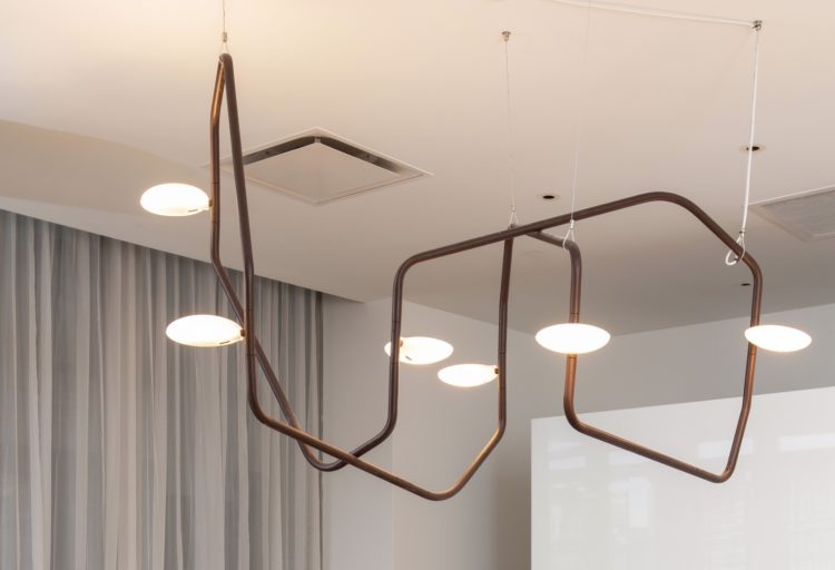 Rich Brilliant Willing Palindrome Chandelier close view of light with gray curtains in the background