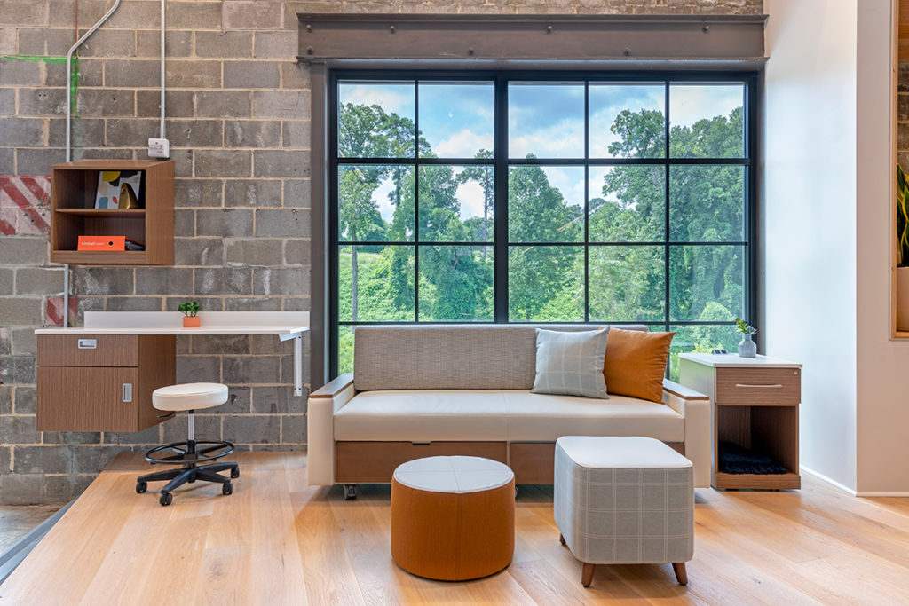 Alterna Casegoods patient room with workspace, sofa, ottomans, and side table