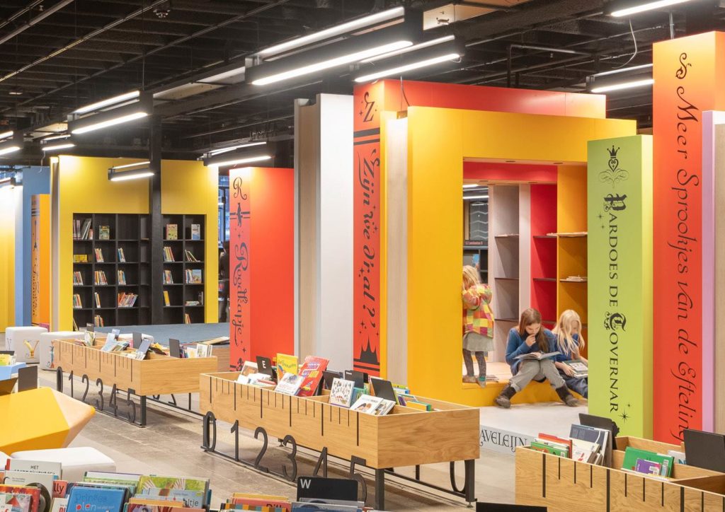 LocHal Public Library children's area with brightly colored bookshelves and wood display cases with three children reading
