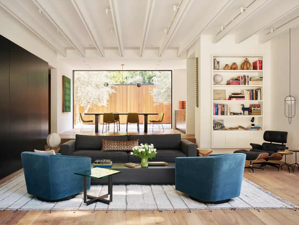 Assembledge+ Laurel Hills interior living room with blue chairs and gray sofa on white rug on light wood floors with dining area in background