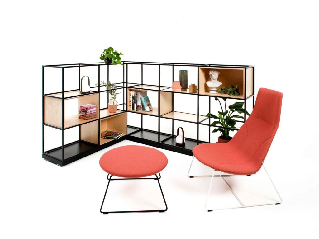 Spacestor Palisades II partition walls steel-frame system with shelving components holding books, plants, and other items behind orange lounge and ottoman