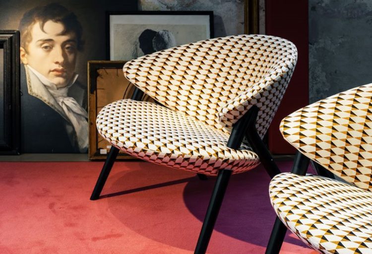 Zanotta's Oliva Chair front/side view two chair off white, orange, black patterned upholstery on red carpet with portrait in background