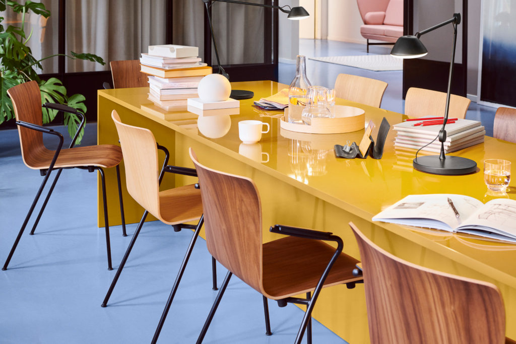 Vico Duo Chair in different woods at conference table with books and glasses of water and a lamp