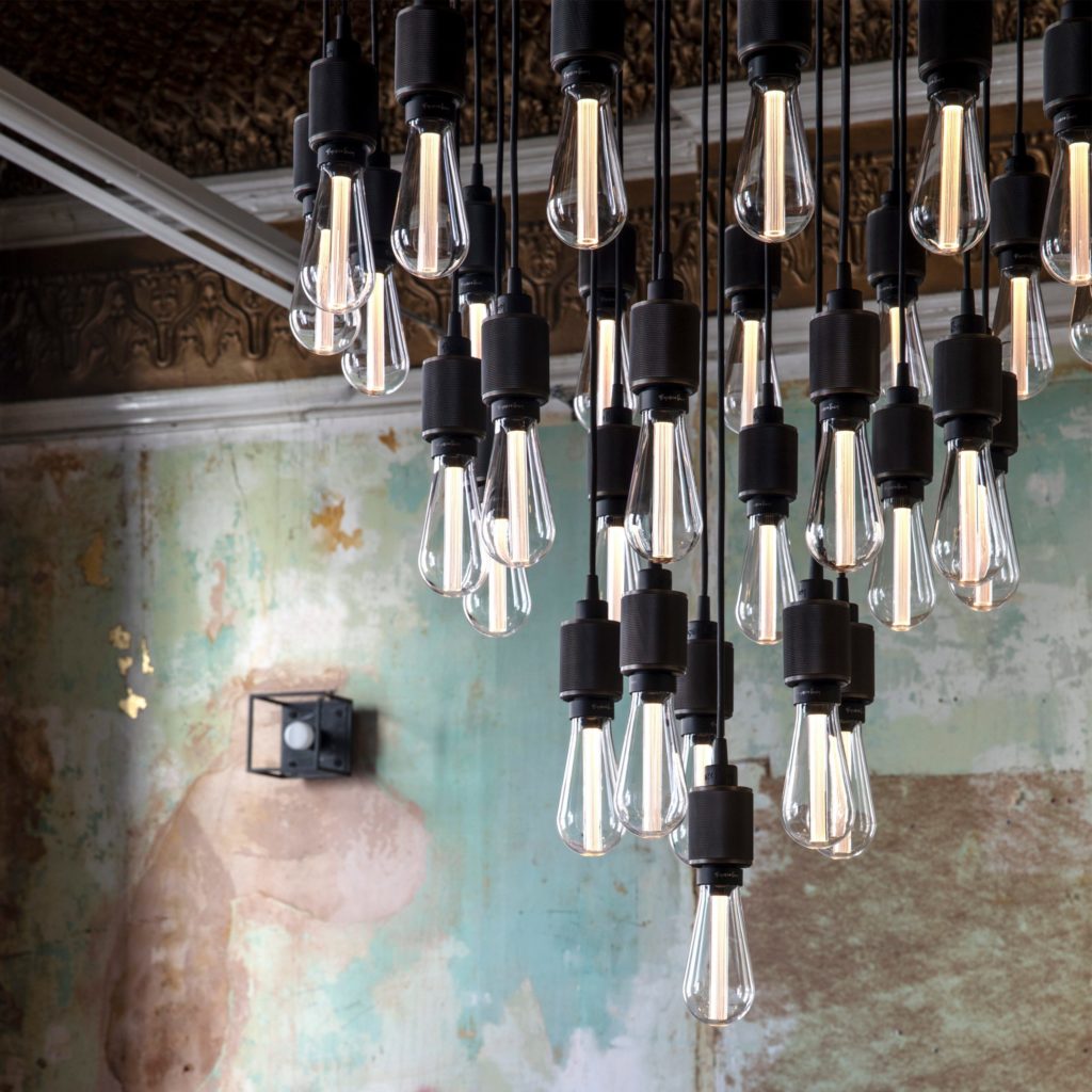 Buster Bulb cluster of crystal color in chandelier form with distress painted wall in backgroung