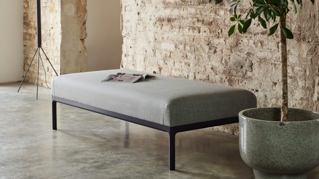 Pearson Lloyd Edge collection ottoman in gray against brick wall