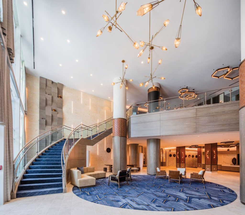 H.E. Williams Lighting chandeliers with thin rods at different angles and spherical lamps in foyer with winding staircase