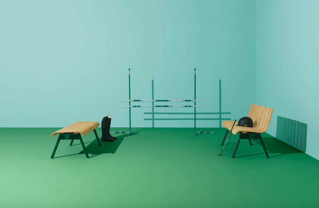 Ethimo Ace at equestrian center with long bench and backless bench, rider's boots, and horse jumping obstacle on green floor