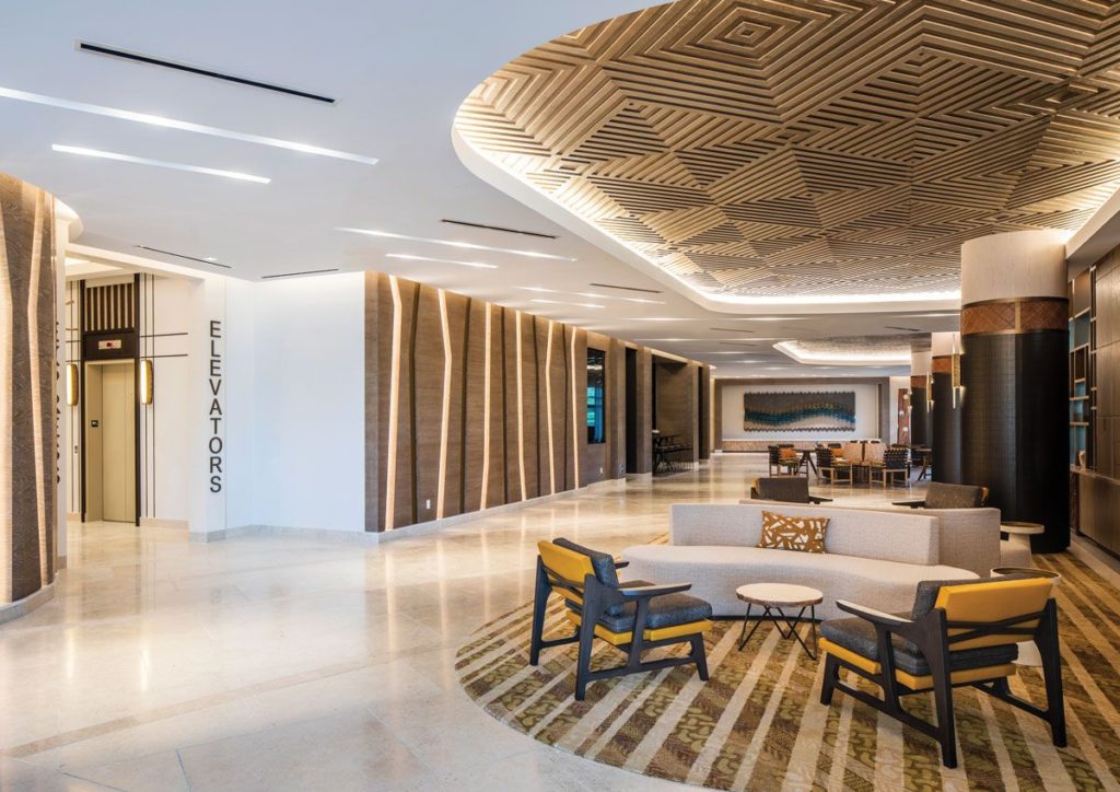 H.E. Williams Lighting common area near elevators with linear recessed lighting and vertical lighting on wall with chairs and sofas