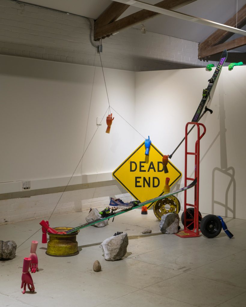 Launch Pad Dead End found objects with disembodied hands, dead end sign, metal dolly, rocks and other objects