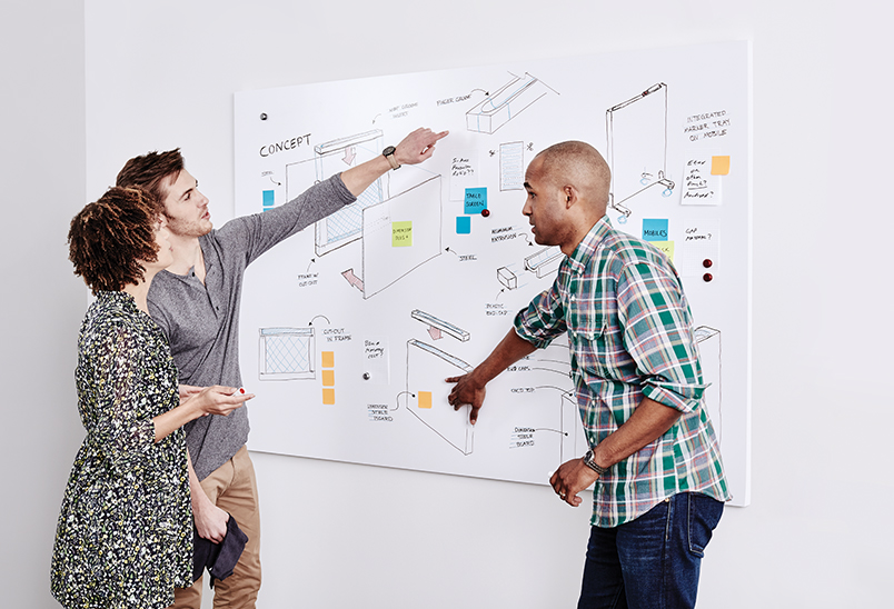 Three people talking about drawings on a glass board