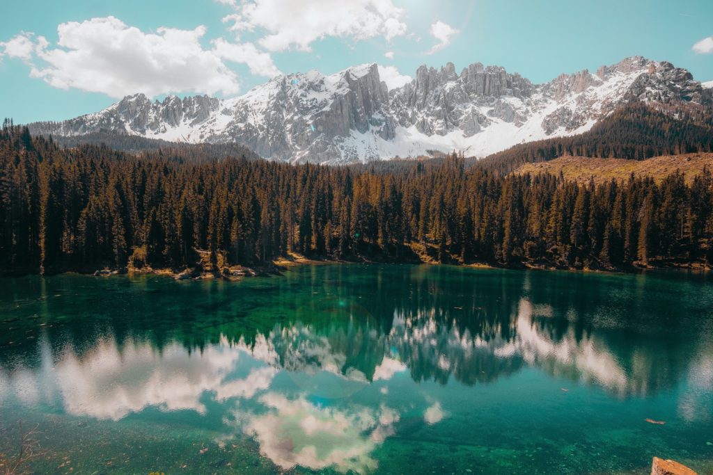 Mountain scene with peaks, trees, and blue water reflecting mountain and trees