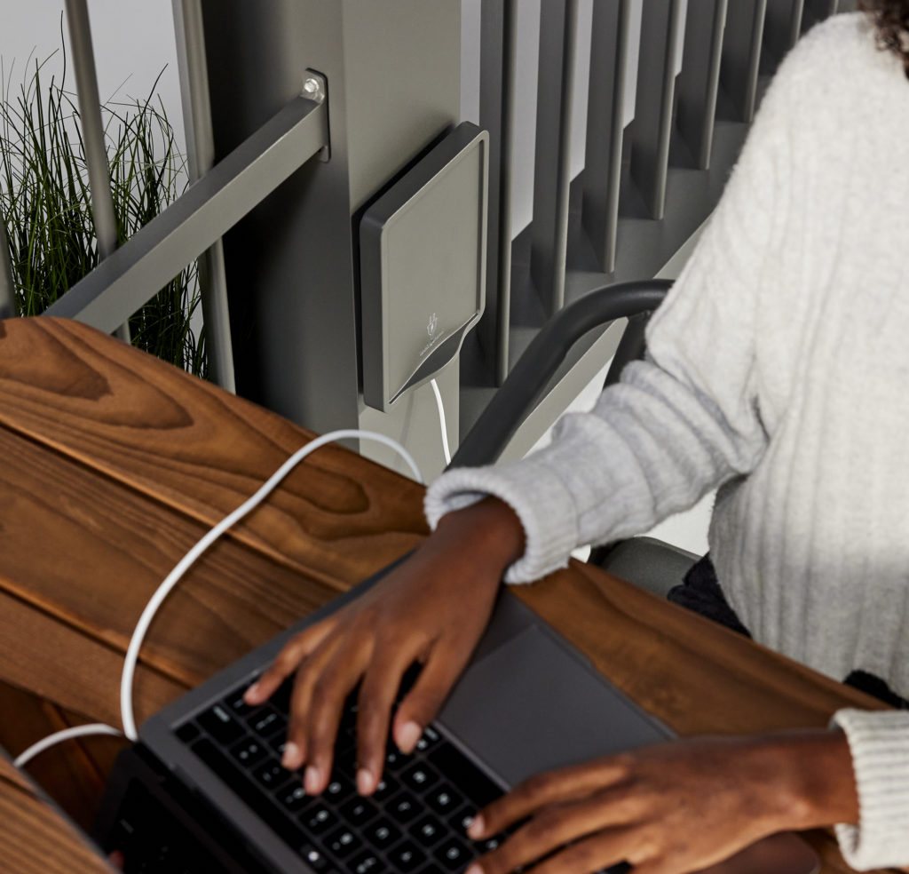 detail of computer with hands on keyboard atop wooden table and integrated power