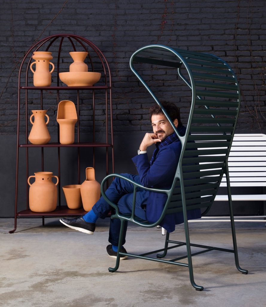 Dark green chair with Hayon sitting in it near shelf of terracotta vases