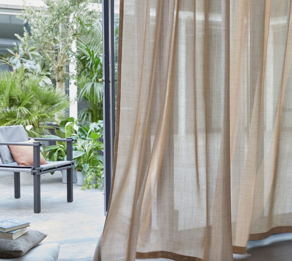 Window fabric flowing and transparent in light brown with veranda visible beyond