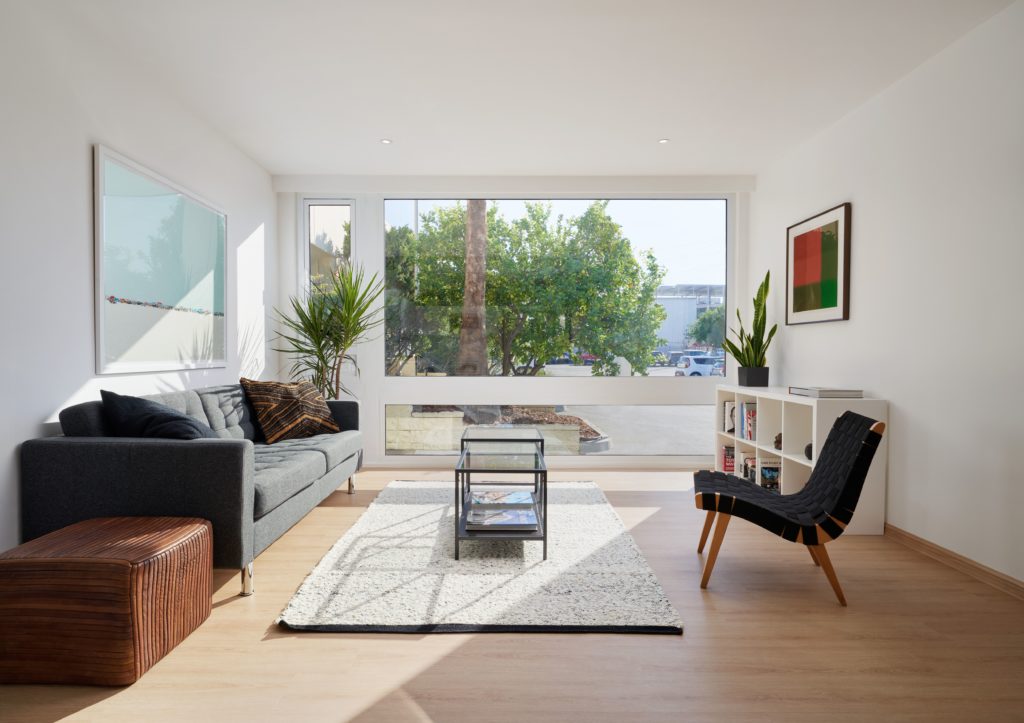 Interior of apartment pod with comfy couch, modern table, designer Scandinavian chair with view looking out on palm tree and bushes