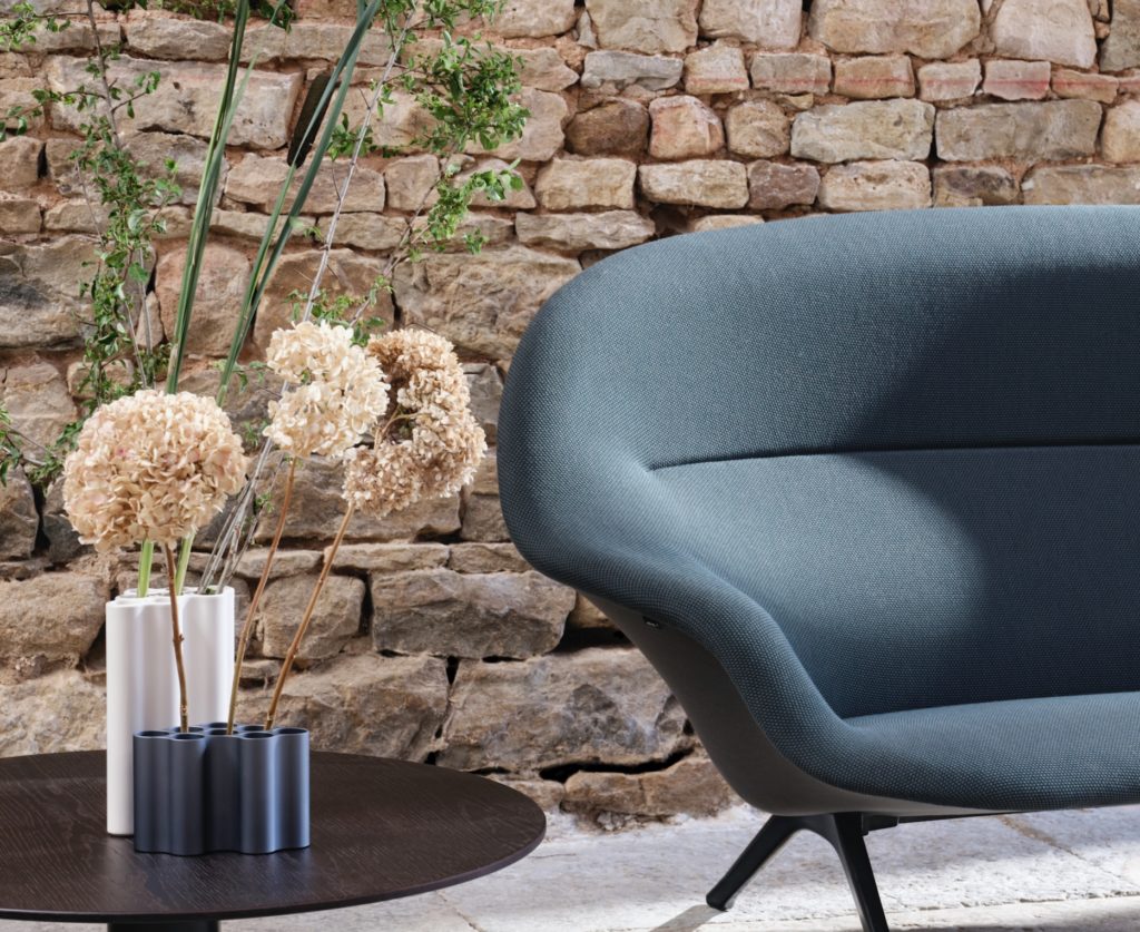 Partial view of blue sofa with stone wall background and vases with dried flowers next to it