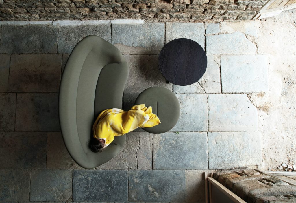 Abalon sofa from above with person wrapped in blanket, also ottoman in matching dark green and black table on stone floor
