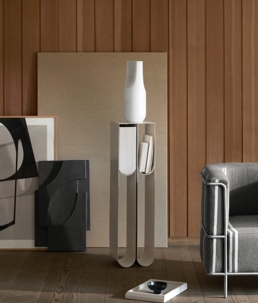 Curved pedestal with white vase, books in one of the compartments, near sofa