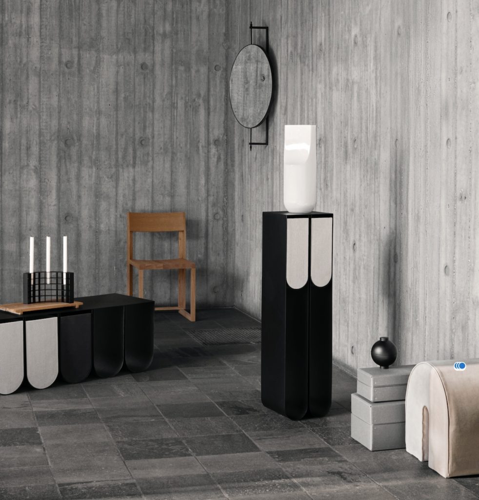 Curved pedestal in black with white vase on top in minimal room with stone floor and concrete wall