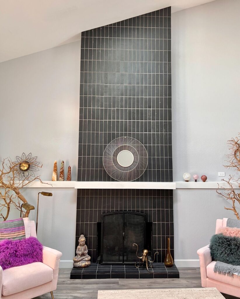 vertically oriented black tile from floor to ceiling with fireplace, pink chairs, and various accessories on fireplace ledge